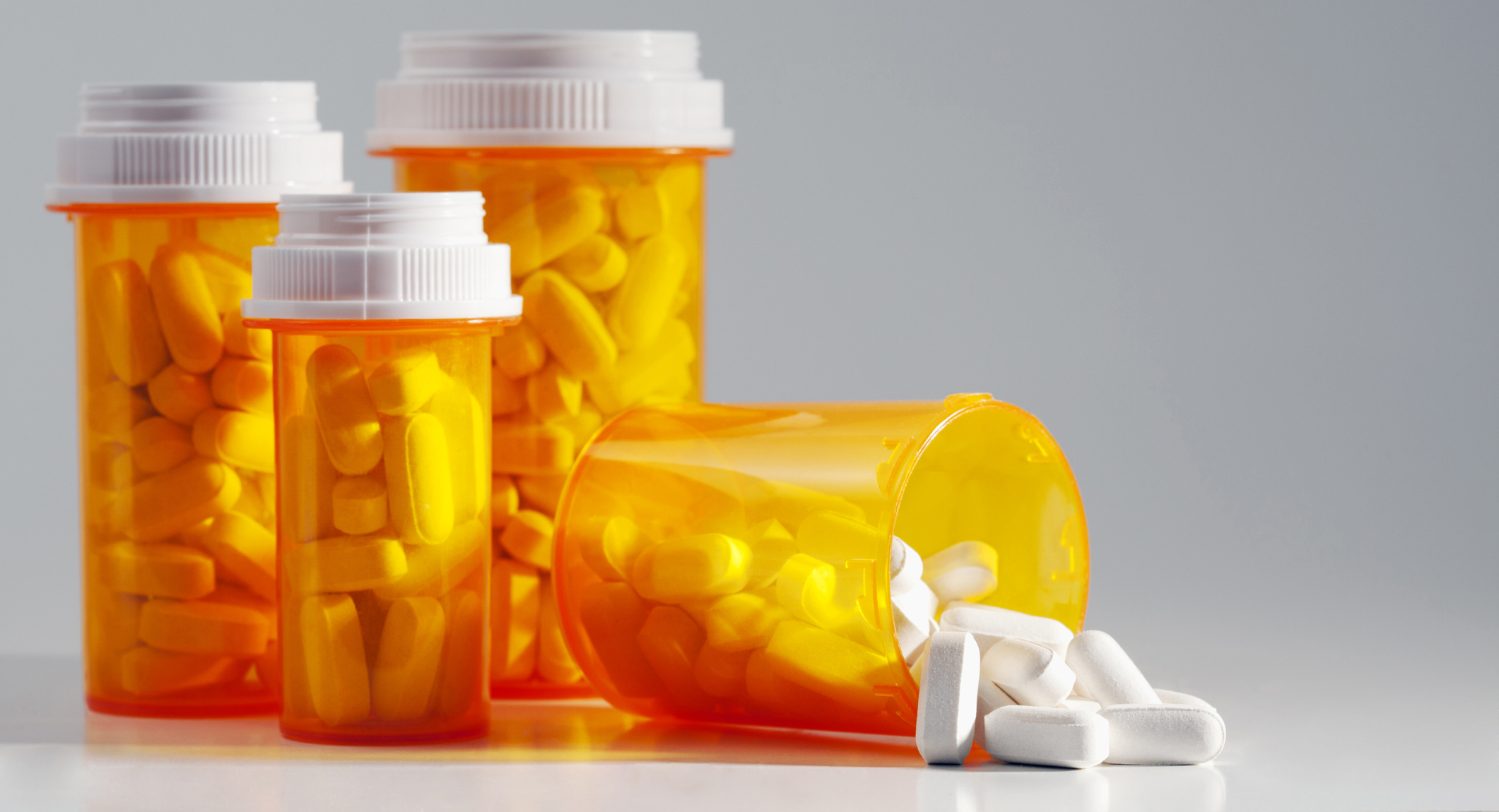 Prescription medication spilling from an open bottle. This macro shot shows caplets or pills in the opening of a medicine bottle with other standing bottles in the background.