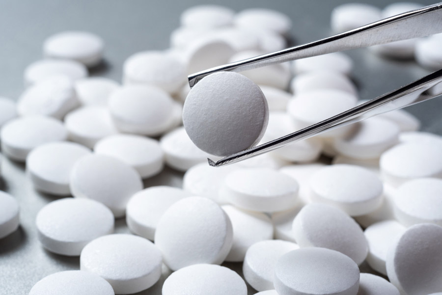 Picture of white pills in background with one pill held up with tweezers in foreground.